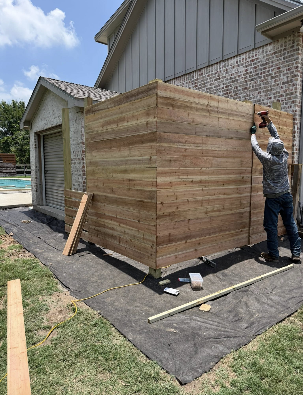 Craftsman installing a horizontal cedar enclosure beside a home