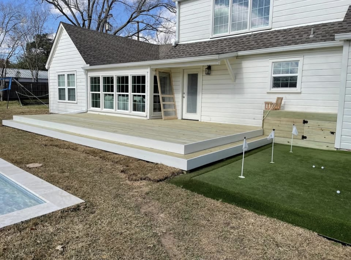 Low-profile wood deck next to a backyard putting green and pool