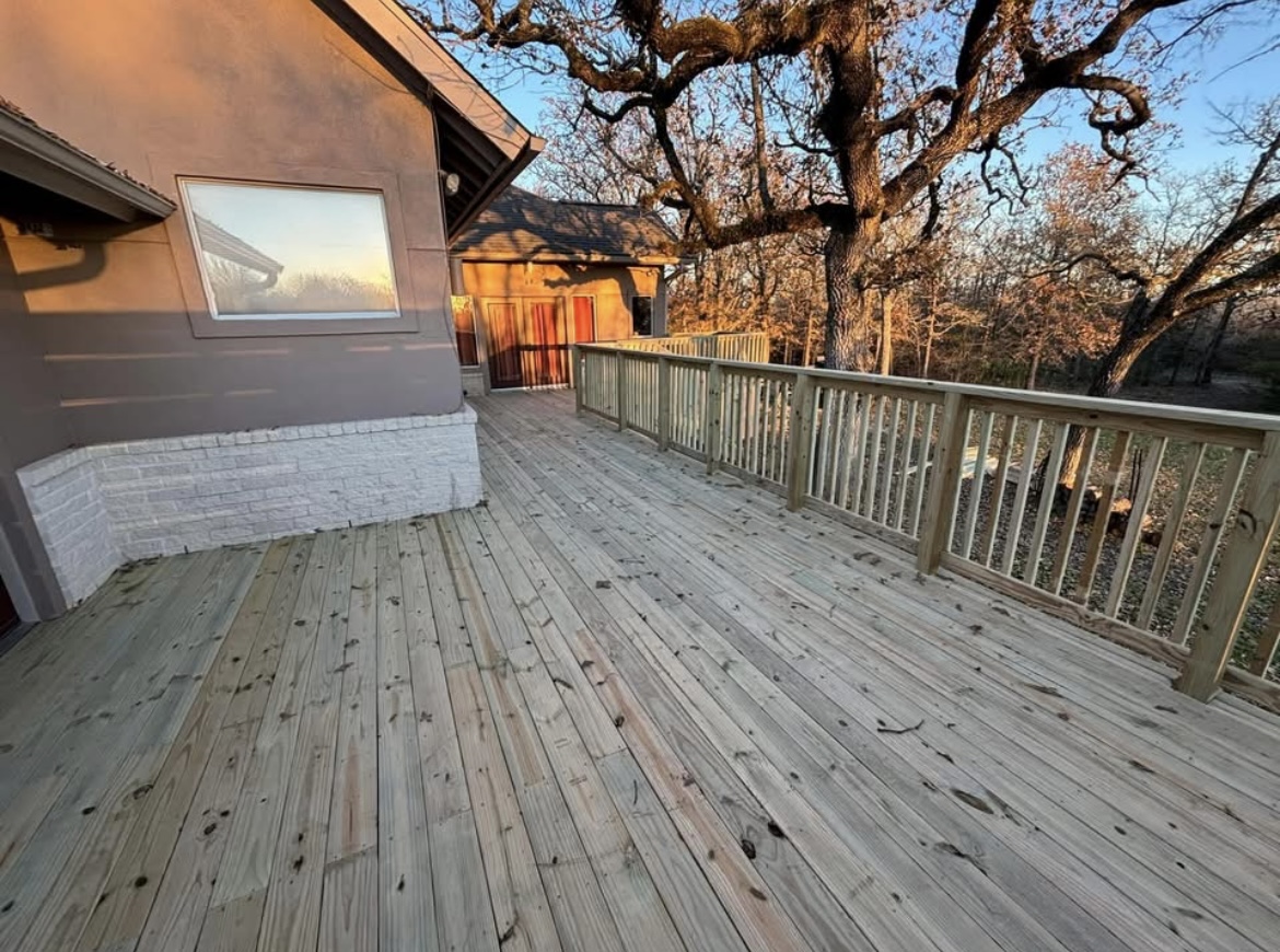 Large wood deck with railing overlooking oak trees at sunset