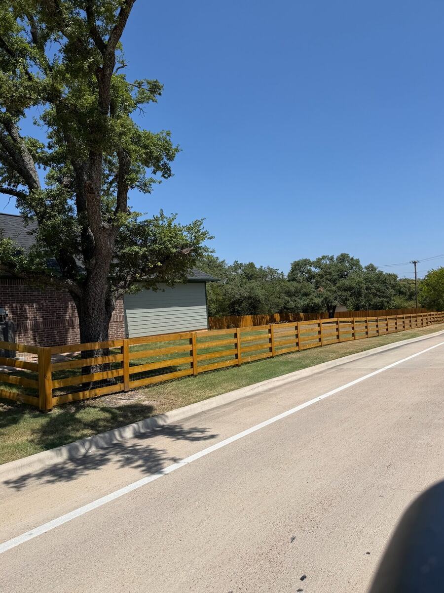 Custom wood rail fence with wire mesh installed along a roadside property