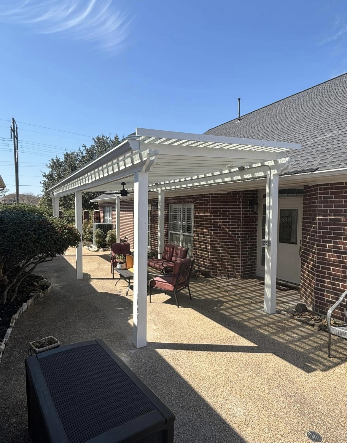 White pergola patio cover over a concrete patio on a brick home